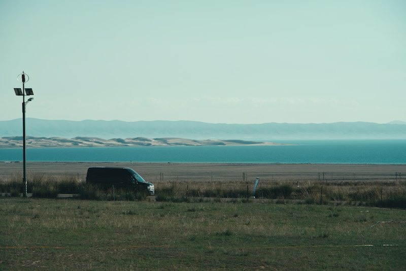 A black van on a road near a blue lake and distant mountains