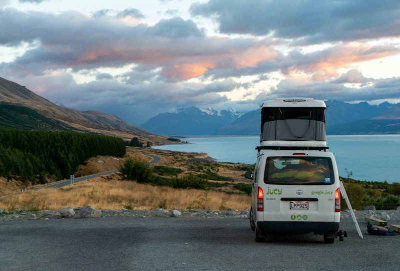 A camper van parked above a lake at dusk, mountains behind